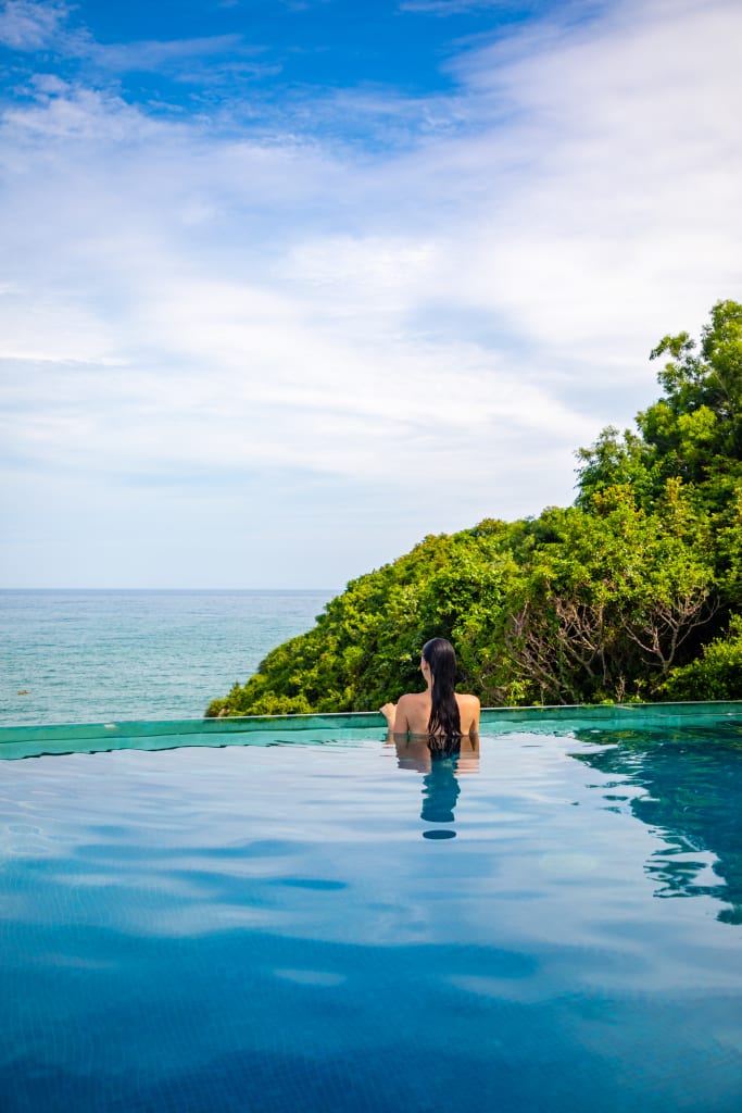 Woman relaxing in infinity swimming pool with sea view, vacation in tropical country